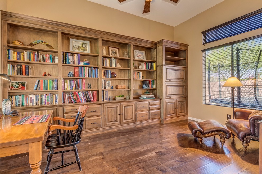 Modelo de despacho de estilo americano de tamaño medio con biblioteca, paredes beige, suelo de madera en tonos medios, escritorio independiente y suelo marrón