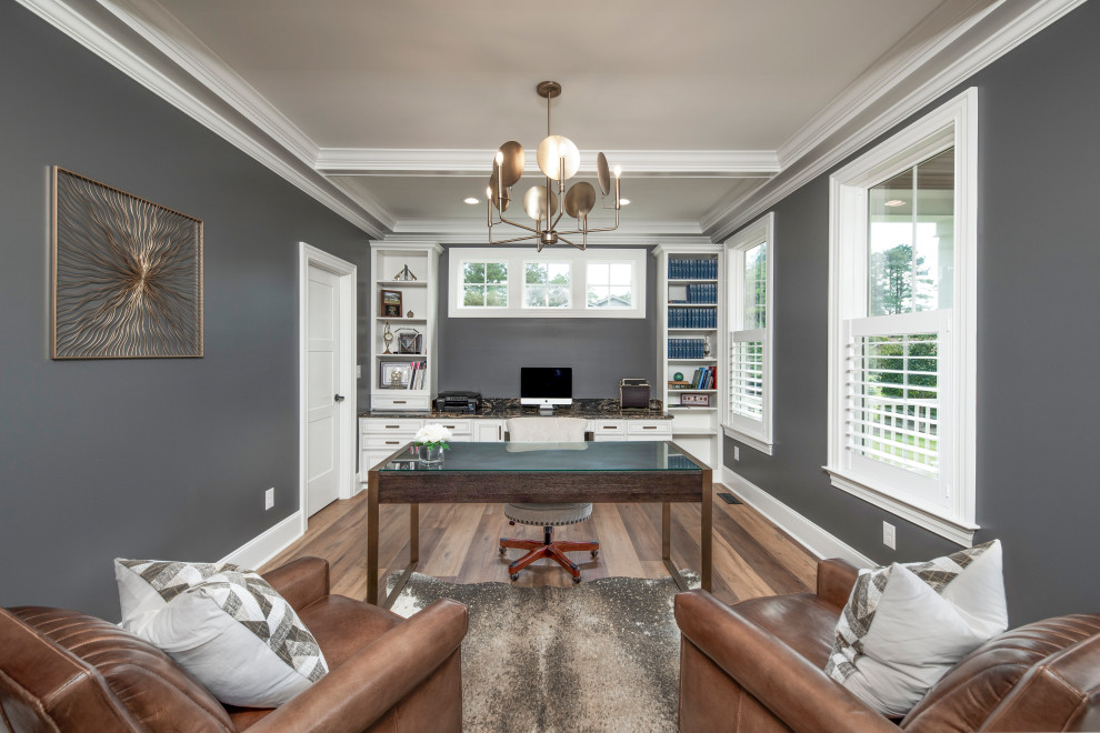 Großes Klassisches Arbeitszimmer mit Arbeitsplatz, grauer Wandfarbe, braunem Holzboden, freistehendem Schreibtisch und braunem Boden in Sonstige