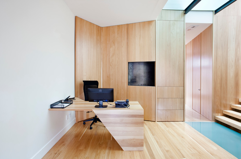 Modernes Arbeitszimmer mit weißer Wandfarbe, braunem Holzboden und Einbau-Schreibtisch in Montreal