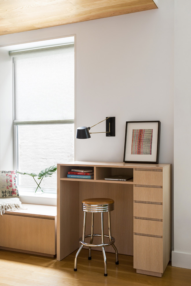 Modern inredning av ett mellanstort hemmabibliotek, med vita väggar, mellanmörkt trägolv, ett inbyggt skrivbord och grått golv