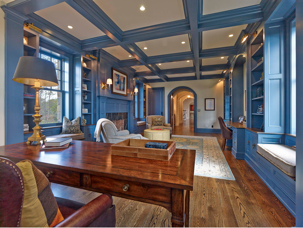 Großes Klassisches Arbeitszimmer mit Arbeitsplatz, blauer Wandfarbe, braunem Holzboden, Kamin, Kaminumrandung aus Stein, freistehendem Schreibtisch und braunem Boden in Philadelphia
