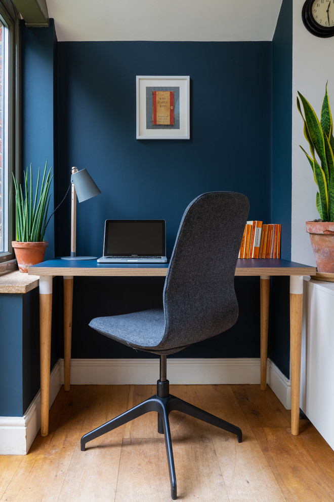 Kleines Stilmix Arbeitszimmer mit Arbeitsplatz, blauer Wandfarbe, braunem Holzboden und freistehendem Schreibtisch in London