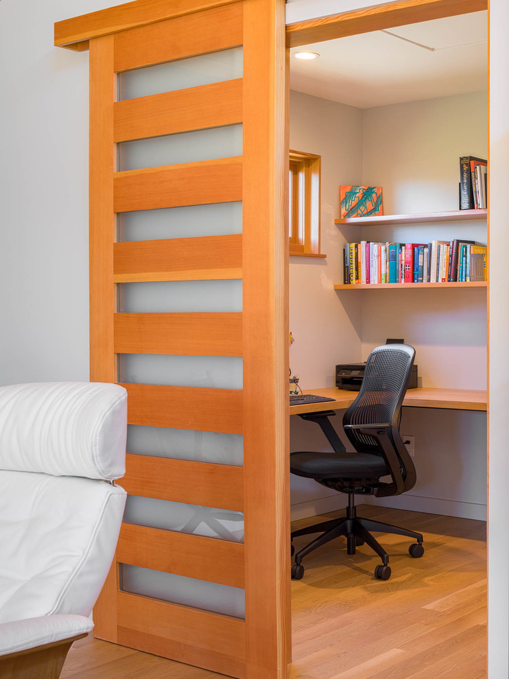 Modelo de despacho contemporáneo de tamaño medio sin chimenea con paredes grises, suelo de madera clara, escritorio empotrado y suelo beige