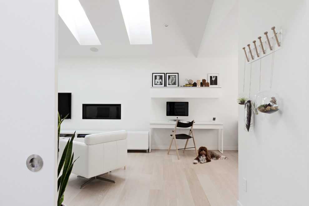 Imagen de despacho contemporáneo con paredes blancas, suelo de madera clara, chimenea lineal y escritorio independiente