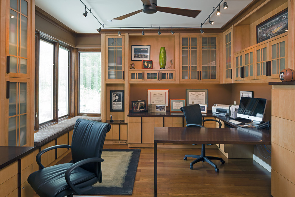 Exempel på ett amerikanskt arbetsrum, med bruna väggar, mellanmörkt trägolv och ett inbyggt skrivbord