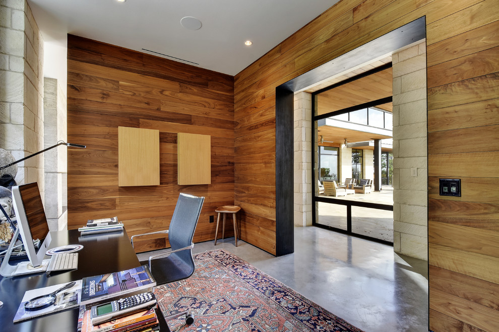 This is an example of a contemporary study in Austin with brown walls, concrete flooring and a freestanding desk.
