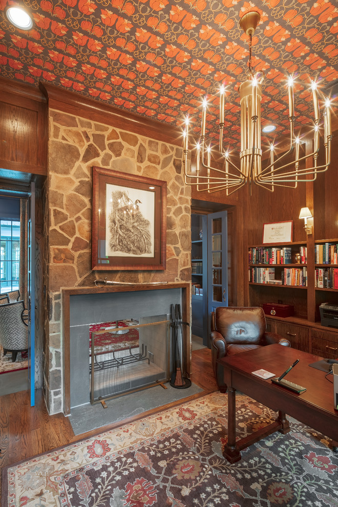 Idée de décoration pour un grand bureau tradition avec une bibliothèque ou un coin lecture, un mur marron, un sol en bois brun, une cheminée double-face, un manteau de cheminée en pierre, un bureau indépendant et un sol marron.