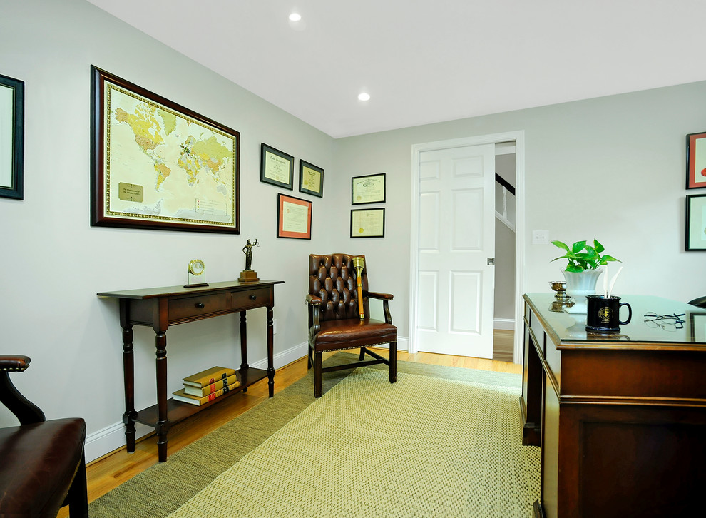 Ejemplo de despacho clásico de tamaño medio con paredes grises, suelo de madera clara y escritorio independiente