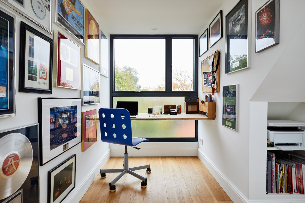 Photo of a contemporary home office in Surrey with white walls, medium hardwood flooring, a built-in desk and brown floors.