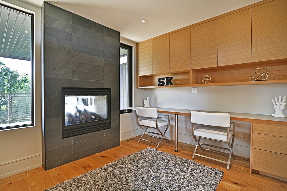 Bild på ett stort funkis arbetsrum, med vita väggar, ljust trägolv, en standard öppen spis, en spiselkrans i trä, ett inbyggt skrivbord och brunt golv
