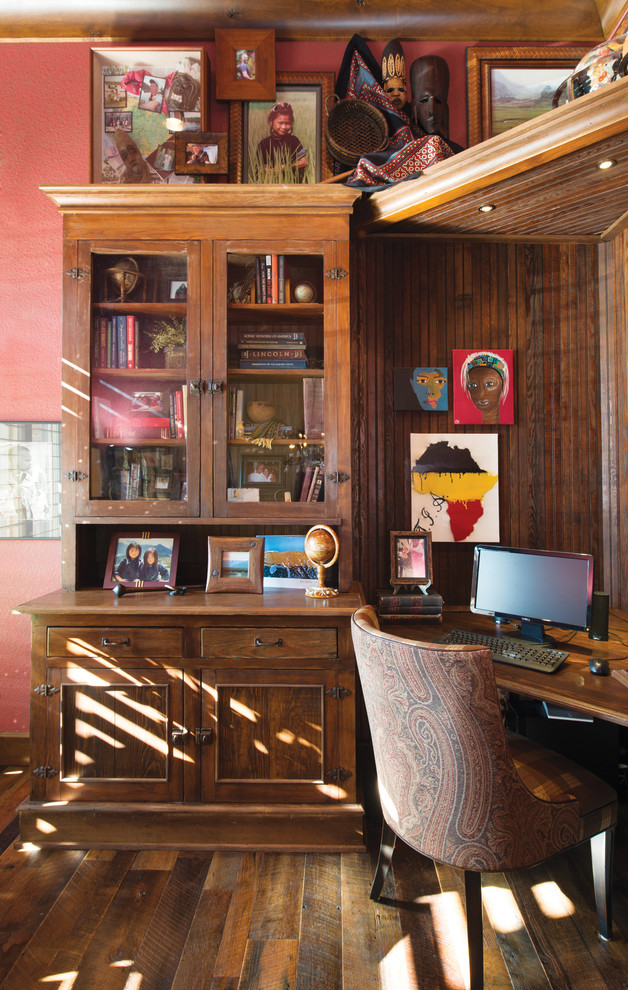 Inredning av ett rustikt mellanstort hemmabibliotek, med röda väggar, mellanmörkt trägolv och ett inbyggt skrivbord