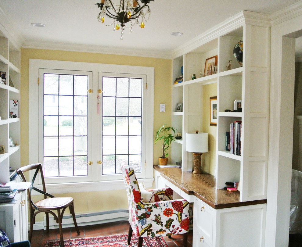 Diseño de despacho tradicional de tamaño medio sin chimenea con biblioteca, paredes amarillas, suelo de baldosas de terracota, escritorio empotrado y suelo rojo