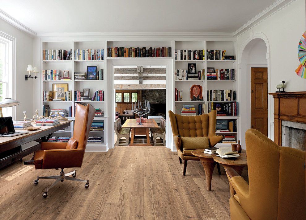 Ejemplo de despacho tradicional renovado con paredes blancas, suelo de madera clara, todas las chimeneas, escritorio independiente, biblioteca y marco de chimenea de piedra