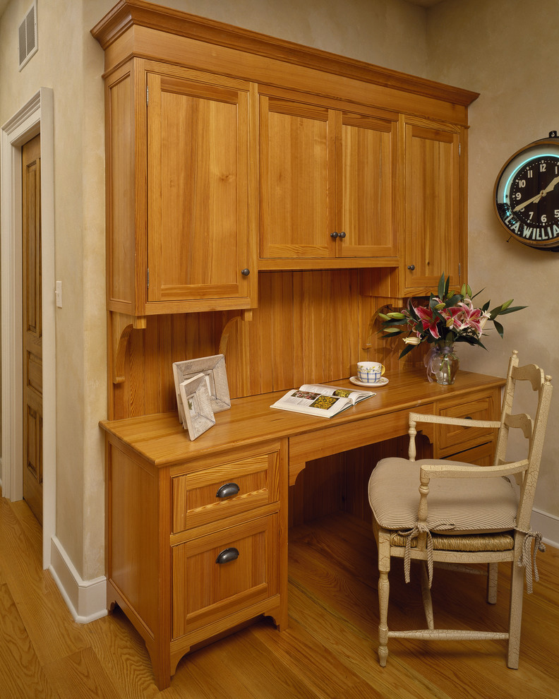Elegant built-in desk medium tone wood floor home office photo in New York with beige walls