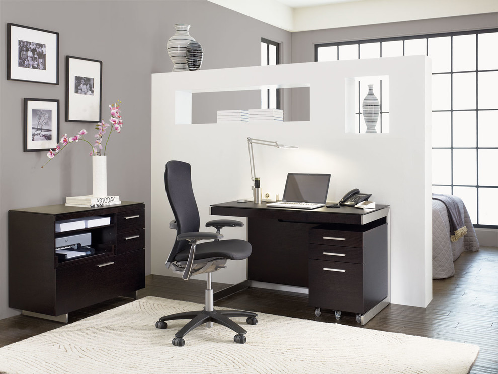 Modelo de despacho minimalista de tamaño medio con paredes grises, suelo de madera en tonos medios y escritorio independiente
