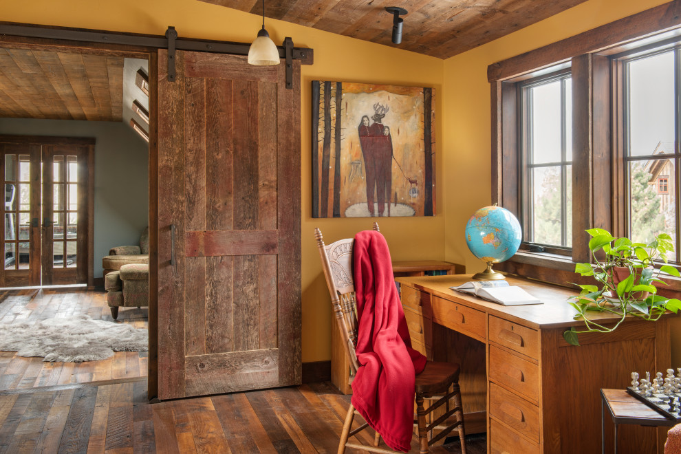 Großes Uriges Arbeitszimmer mit Arbeitsplatz, gelber Wandfarbe, braunem Holzboden, freistehendem Schreibtisch, braunem Boden und Holzdecke in Sonstige