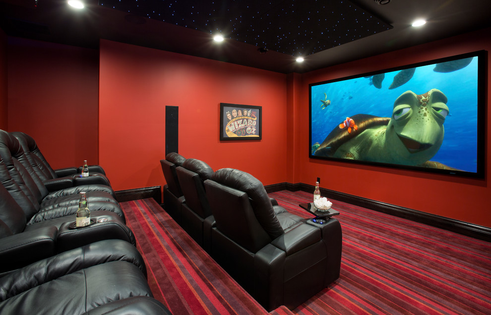 Стильный дизайн: домашний кинотеатр в классическом стиле с красными стенами, ковровым покрытием, проектором и разноцветным полом - последний тренд