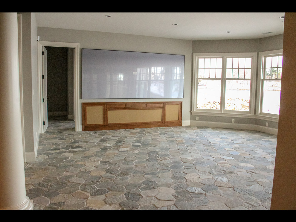 Modelo de cine en casa abierto costero de tamaño medio con paredes grises, suelo de pizarra, televisor colgado en la pared y suelo gris