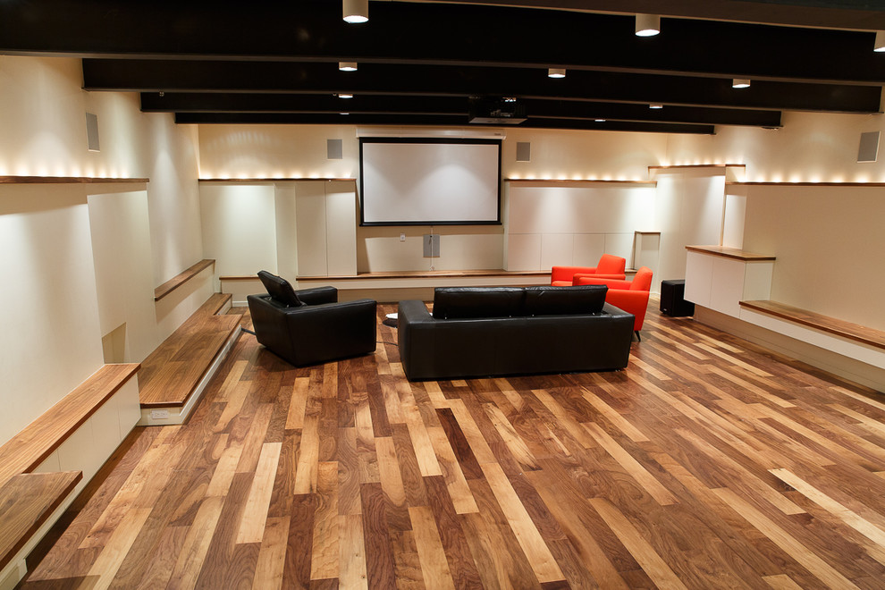 Diseño de cine en casa cerrado actual grande con paredes blancas, suelo de madera en tonos medios y pantalla de proyección