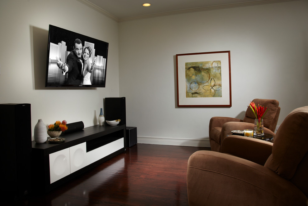 Ejemplo de cine en casa cerrado actual pequeño con paredes blancas, suelo de madera oscura, televisor colgado en la pared y suelo marrón