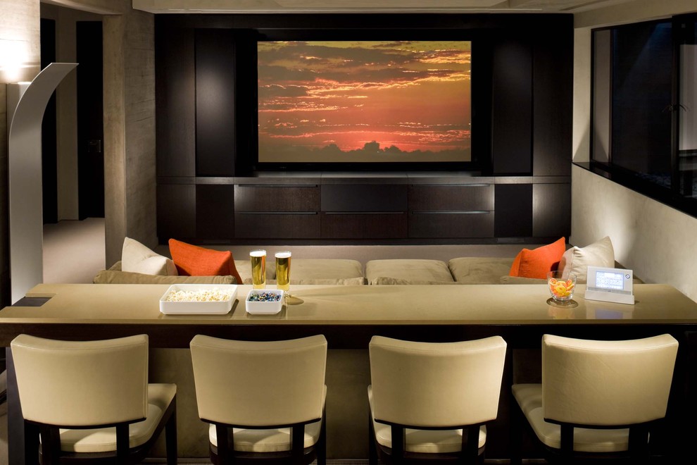 Modelo de cine en casa cerrado actual de tamaño medio con paredes beige, moqueta y pared multimedia