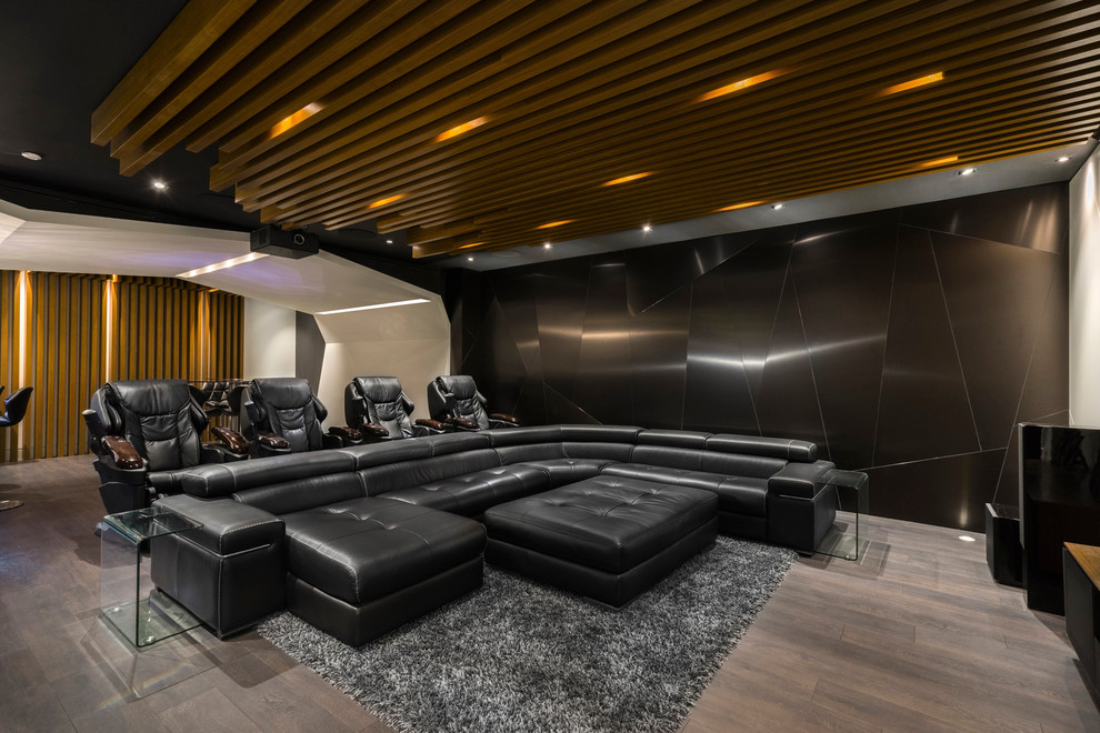 Modelo de cine en casa abierto actual grande con paredes negras, suelo de madera oscura y pantalla de proyección