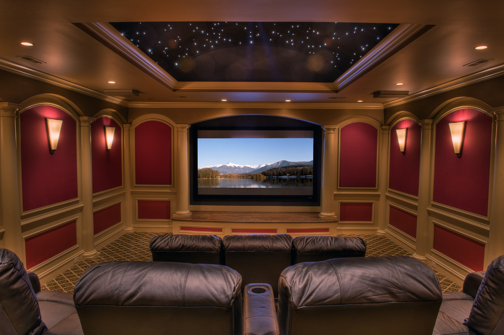 На фото: большой изолированный домашний кинотеатр в классическом стиле с красными стенами, ковровым покрытием, проектором и разноцветным полом с