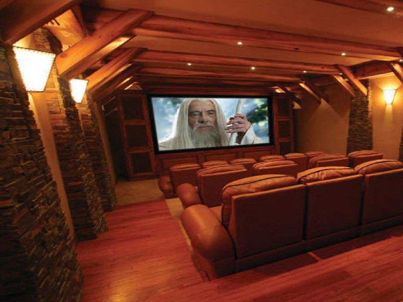 Стильный дизайн: большой открытый домашний кинотеатр в стиле рустика с черными стенами, деревянным полом и телевизором на стене - последний тренд