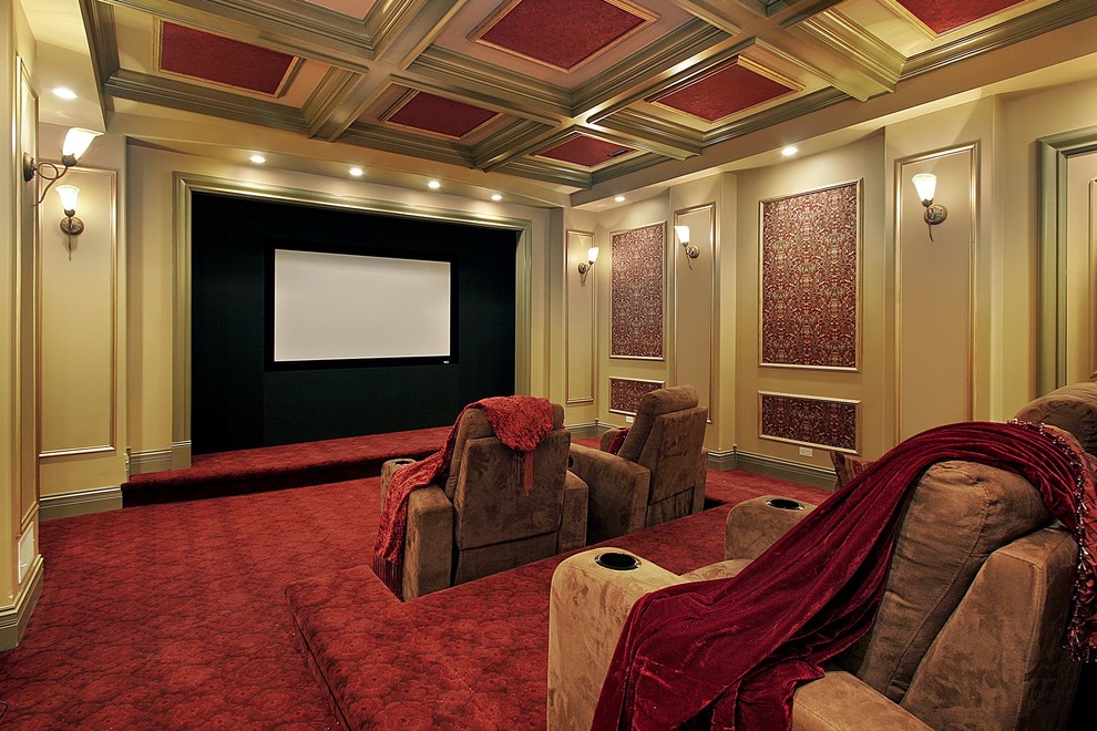 На фото: большой изолированный домашний кинотеатр в классическом стиле с проектором, бежевыми стенами, ковровым покрытием и красным полом с
