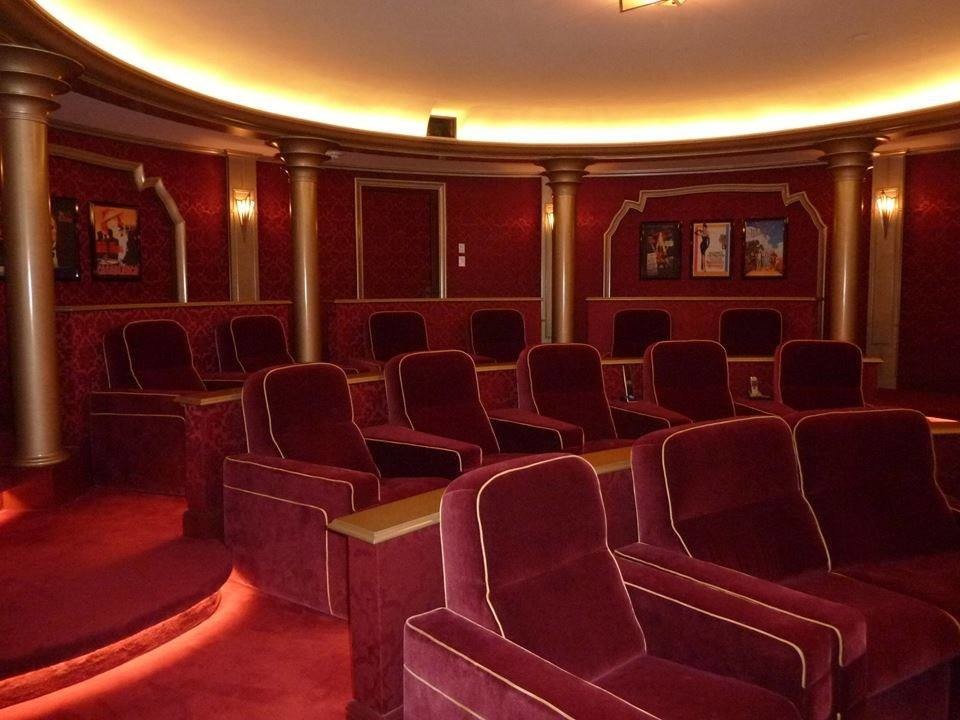 Cette photo montre une très grande salle de cinéma éclectique fermée avec un mur rouge, moquette, un écran de projection et un sol rouge.