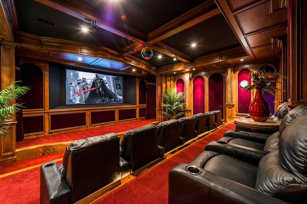 На фото: огромный изолированный домашний кинотеатр в классическом стиле с красными стенами, ковровым покрытием, проектором и красным полом