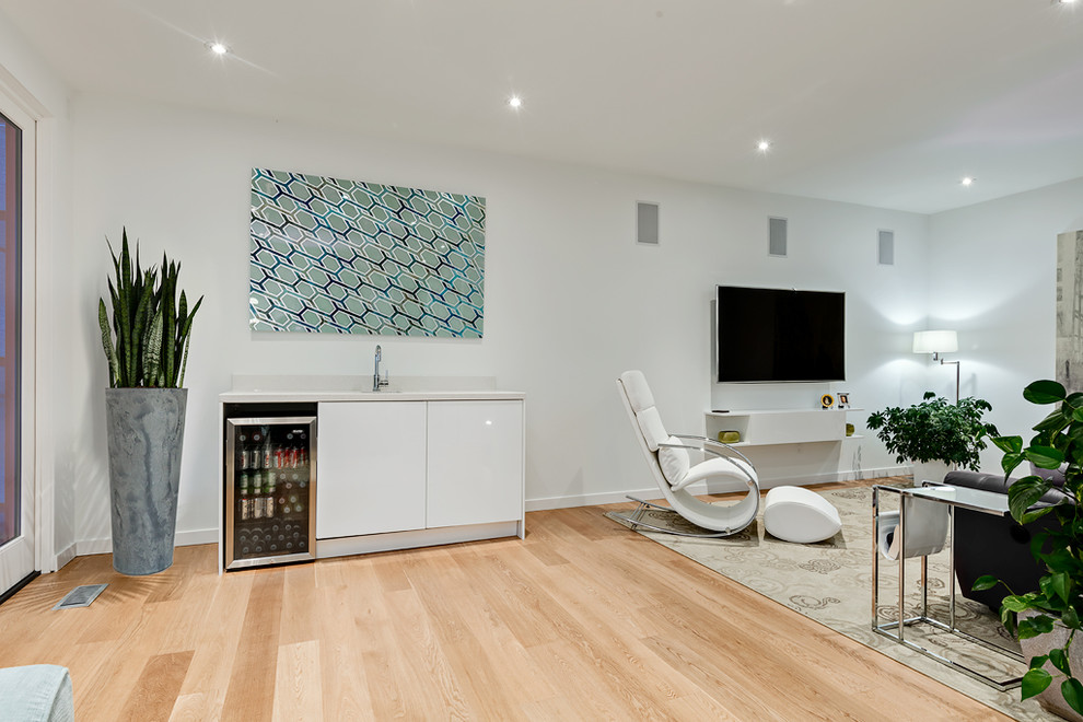 Imagen de cine en casa abierto actual extra grande con paredes blancas, suelo de madera clara y televisor colgado en la pared