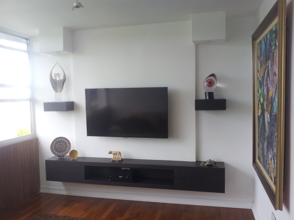 Foto de cine en casa abierto minimalista pequeño con paredes blancas, suelo de madera en tonos medios, televisor colgado en la pared y suelo marrón