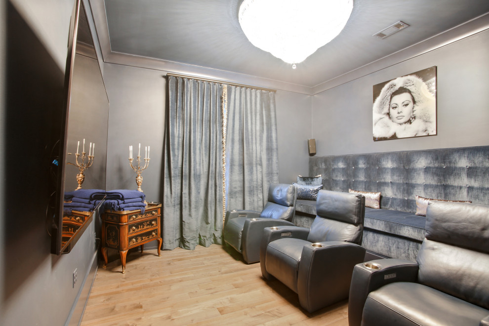 Modelo de cine en casa cerrado clásico renovado pequeño con paredes grises, suelo de madera clara, televisor colgado en la pared y suelo marrón