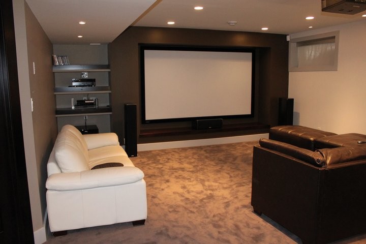 This is an example of a large classic enclosed home cinema in Other with beige walls, carpet, a projector screen and brown floors.