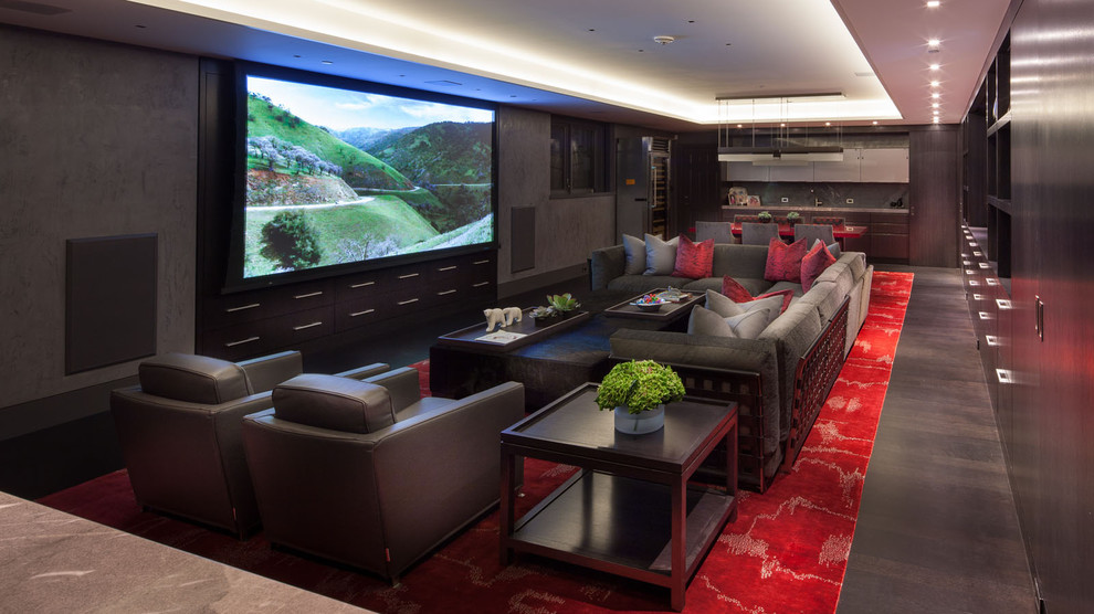 Aménagement d'une très grande salle de cinéma contemporaine ouverte avec un mur gris, parquet foncé, un écran de projection et un sol rouge.