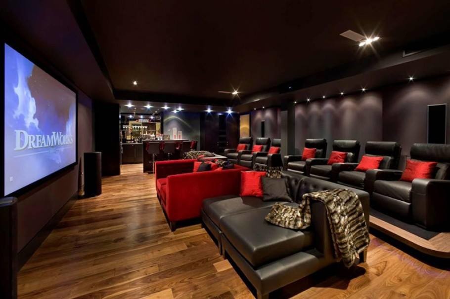 Cette image montre une très grande salle de cinéma minimaliste ouverte avec un mur violet, un sol en bois brun et un écran de projection.