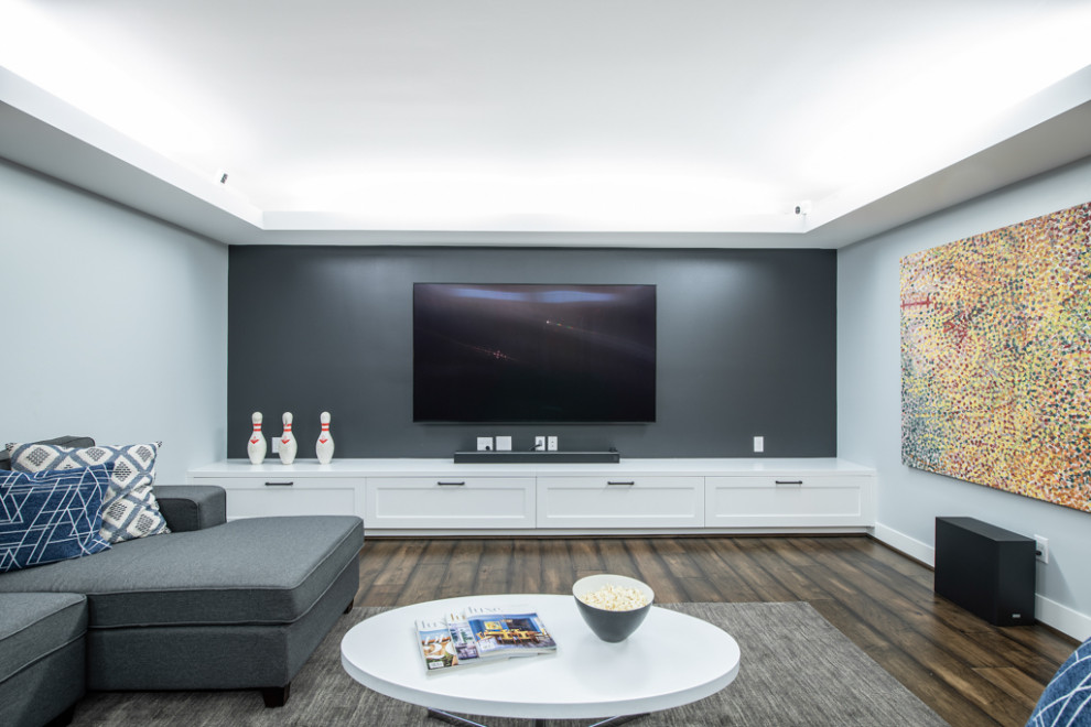 Foto de cine en casa abierto de estilo americano grande con paredes grises, suelo de madera en tonos medios, televisor colgado en la pared y suelo multicolor