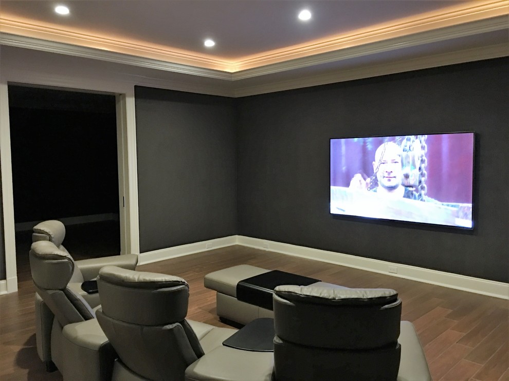 This is an example of a large traditional enclosed home cinema in New York with grey walls, medium hardwood flooring, a wall mounted tv and brown floors.