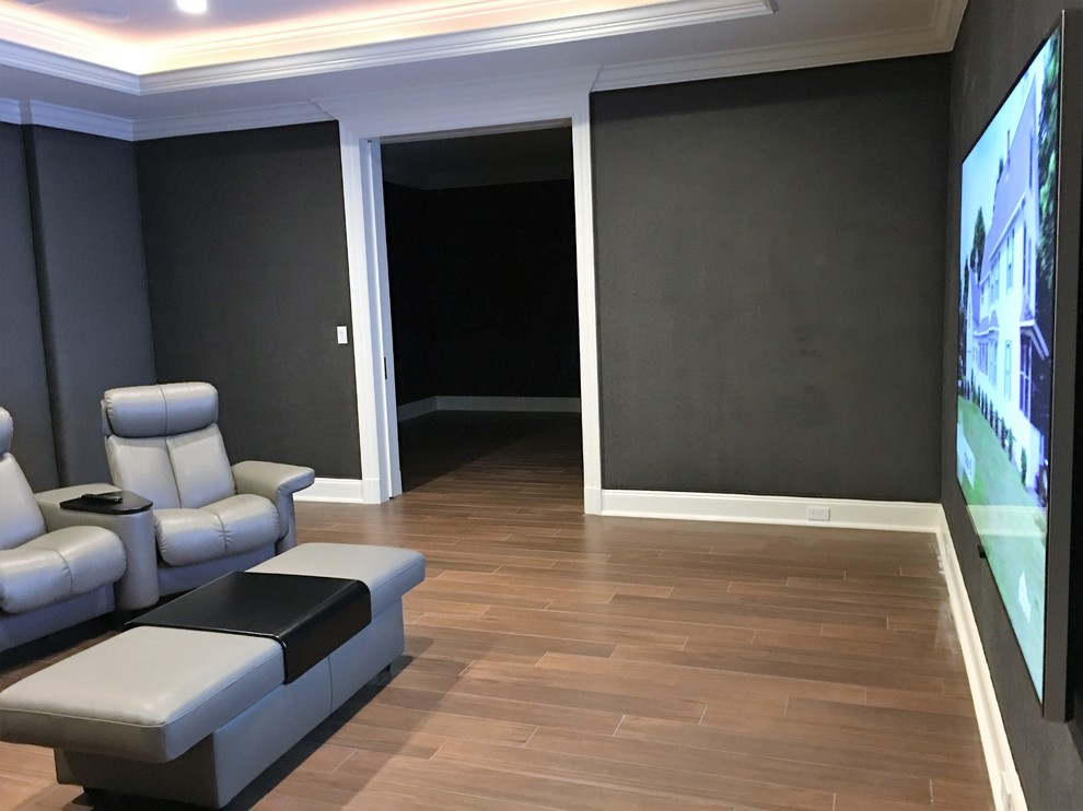 Immagine di un grande home theatre tradizionale chiuso con pareti grigie, pavimento in legno massello medio, TV a parete e pavimento marrone