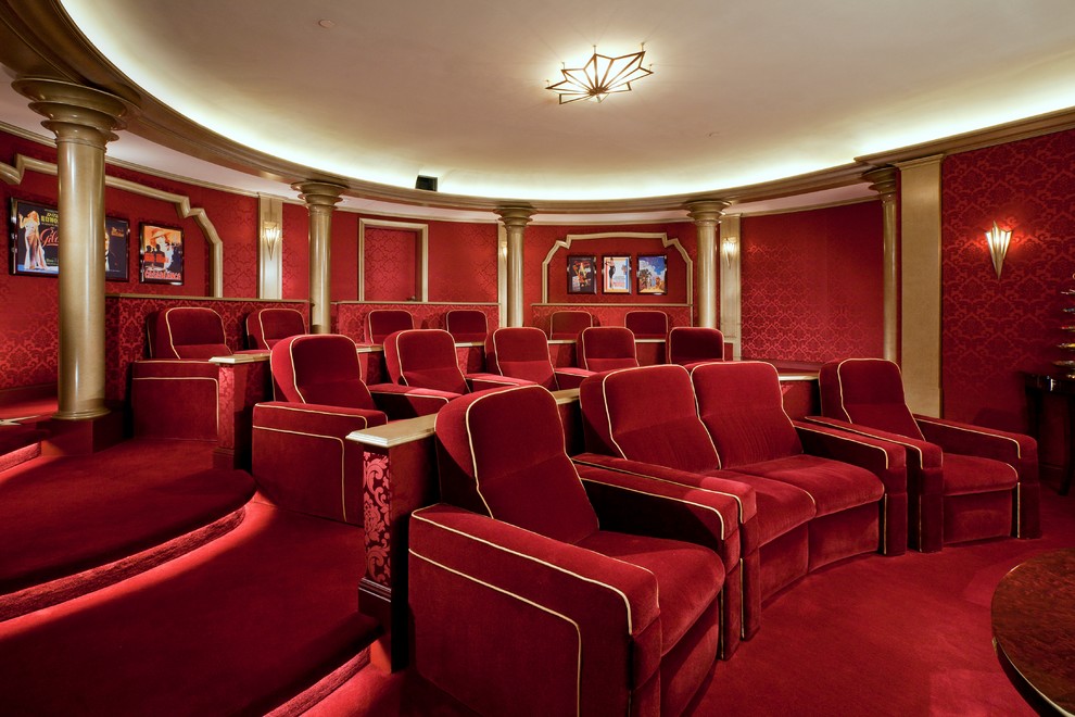 На фото: большой изолированный домашний кинотеатр в викторианском стиле с красными стенами, ковровым покрытием, проектором и красным полом