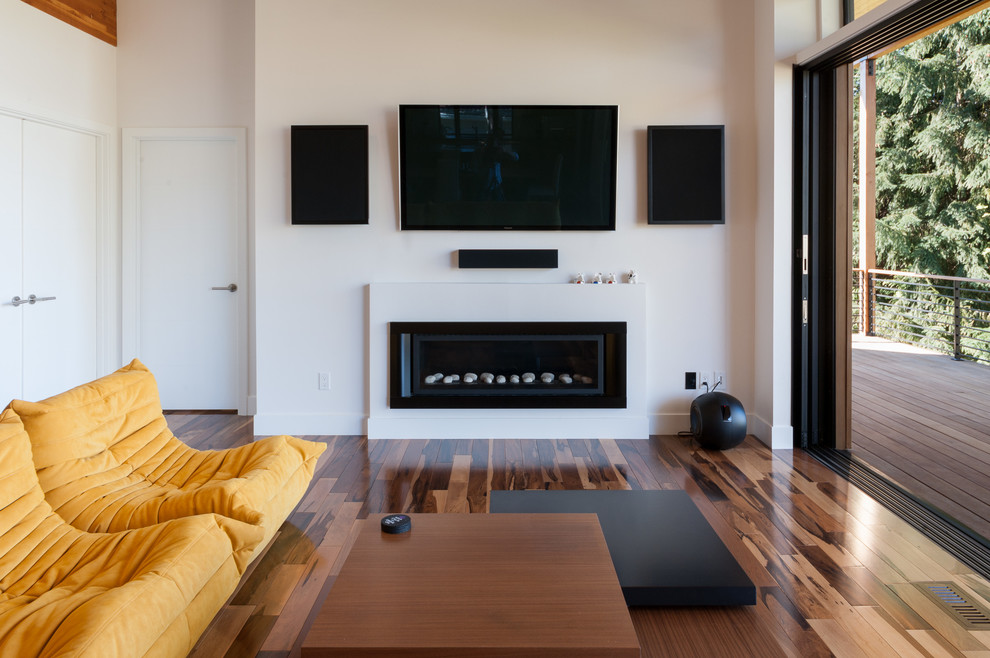 Imagen de cine en casa abierto actual de tamaño medio con paredes blancas, suelo de madera en tonos medios y televisor colgado en la pared