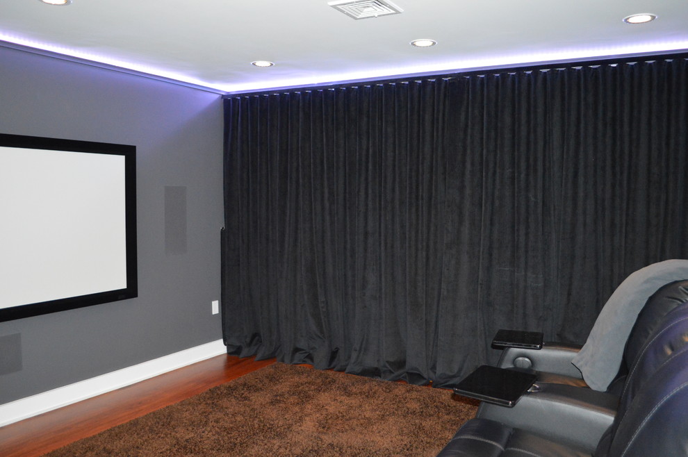 Example of a mid-sized trendy enclosed dark wood floor and brown floor home theater design in Boston with gray walls and a media wall