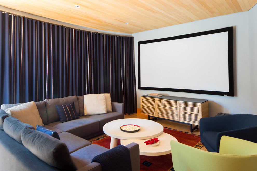 Modelo de cine en casa cerrado minimalista de tamaño medio con paredes grises, suelo de madera clara, pantalla de proyección y suelo marrón