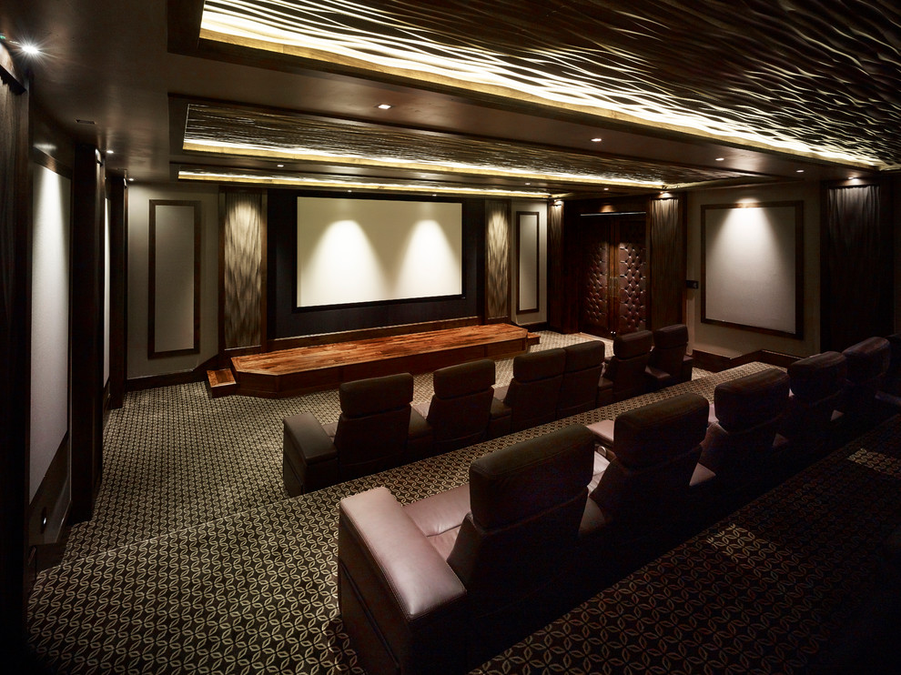 На фото: огромный изолированный домашний кинотеатр в классическом стиле с коричневыми стенами, ковровым покрытием, проектором и разноцветным полом