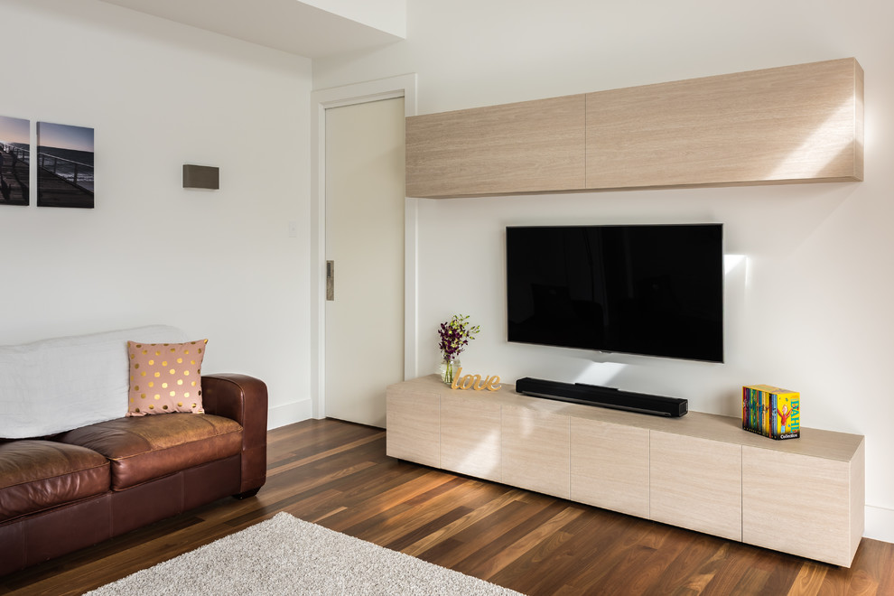 Modelo de cine en casa cerrado actual pequeño con paredes blancas, suelo de madera en tonos medios y televisor colgado en la pared