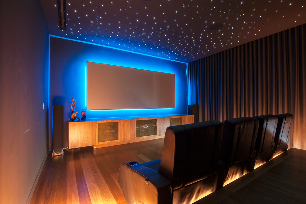 Modelo de cine en casa cerrado actual con paredes grises, suelo de madera en tonos medios, televisor colgado en la pared y suelo blanco