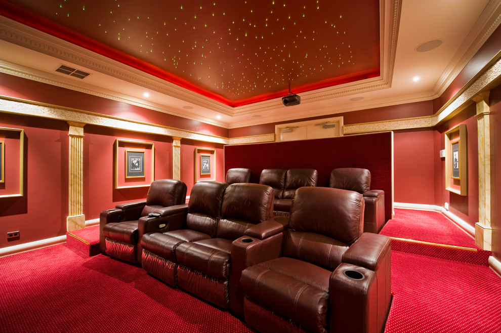 Стильный дизайн: большой изолированный домашний кинотеатр в классическом стиле с красными стенами, ковровым покрытием, проектором и красным полом - последний тренд