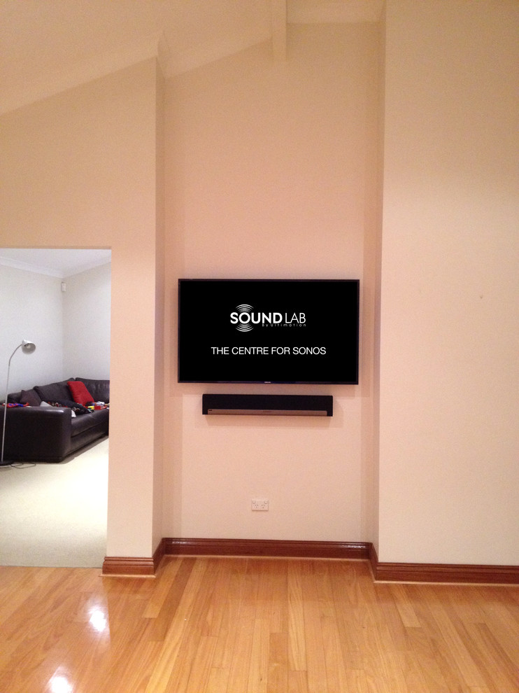 Modelo de cine en casa cerrado actual de tamaño medio con paredes beige, suelo de madera clara y televisor colgado en la pared