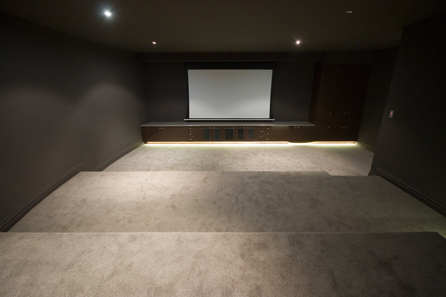Immagine di un ampio home theatre minimalista chiuso con pareti marroni, moquette e schermo di proiezione